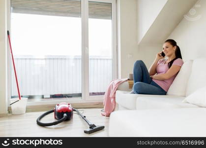 cleaning, household and technology concept - happy woman or housewife calling by smartphone with vacuum cleaner and mop in bucket on floor at home. woman calling by smartphone after cleaning home. woman calling by smartphone after cleaning home