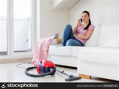 cleaning, household and technology concept - happy woman or housewife calling by smartphone with vacuum cleaner and mop in bucket on floor at home. woman calling by smartphone after cleaning home. woman calling by smartphone after cleaning home