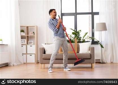 cleaning, housework and housekeeping concept - indian man with broom sweeping floor and singing at home. man with broom cleaning and singing at home