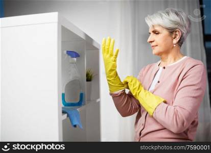 cleaning, housework and housekeeping concept - senior woman putting protective rubber gloves on at home. senior woman putting protective rubber gloves on