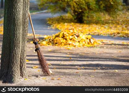 Cleaning in the autumn park - broom with pile of yellow fallen leaves