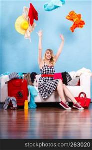Cleaning in the closet, packing for travel, fashion, happiness concept. Woman sitting on sofa throwing up lot of clothes. Clothing flying all over the place. Woman throwing up clothes, clothing flying everywhere