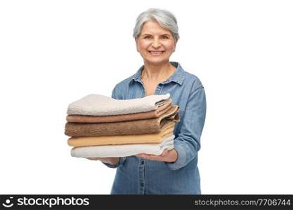 cleaning, laundry and old people concept - portrait of smiling senior woman in denim shirt with pile of clean and folded bath towels over white background. smiling senior woman with clean bath towels