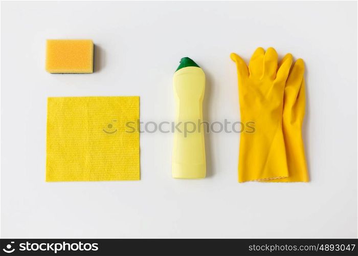 cleaning stuff, housework, housekeeping and household concept - bottle of detergent, rubber gloves with rag and sponge on white background