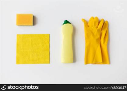 cleaning stuff, housework, housekeeping and household concept - bottle of detergent, rubber gloves with rag and sponge on white background
