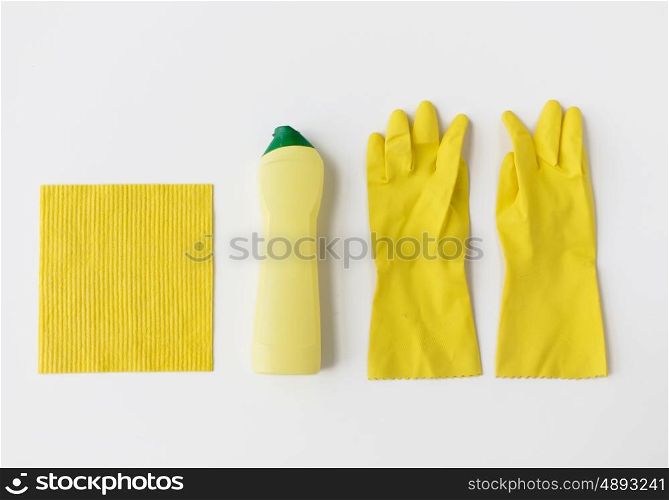 cleaning stuff, housework, housekeeping and household concept - bottle of detergent, rubber gloves and rag on white background