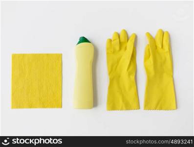 cleaning stuff, housework, housekeeping and household concept - bottle of detergent, rubber gloves and rag on white background
