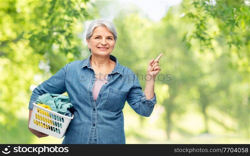 cleaning, wash and old people concept - portrait of smiling senior woman in denim shirt with laundry basket over green natural background. smiling senior woman with laundry basket