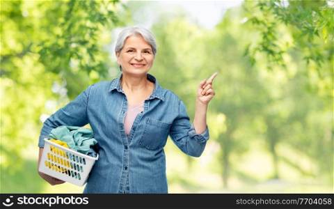 cleaning, wash and old people concept - portrait of smiling senior woman in denim shirt with laundry basket over green natural background. smiling senior woman with laundry basket