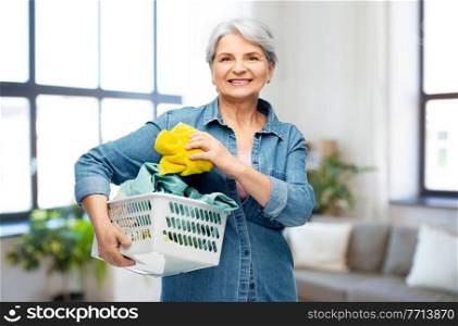cleaning, wash and old people concept - portrait of smiling senior woman in denim shirt with towels in laundry basket over home background. smiling senior woman with laundry basket