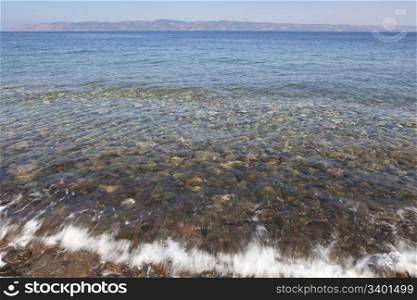 Clear sea water waves washing over pebbles in the Aegean Sea