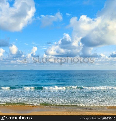 Clear sunny day at seaside. Yellow sand and blue ocean against background of sky.