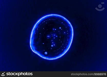 Clear transparent liquid gel dark blue drop or smear with neon light blue flare isolated on dark blue background. Top view. Virus protection or cosmetics concept. Serum texture.. Clear transparent liquid gel dark blue drop or smear with neon light blue flare isolated on dark blue background. Top view. Virus protection or cosmetics concept. Serum texture