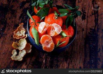Clementines with leaves in a blue ceramic dish on an old wooden table