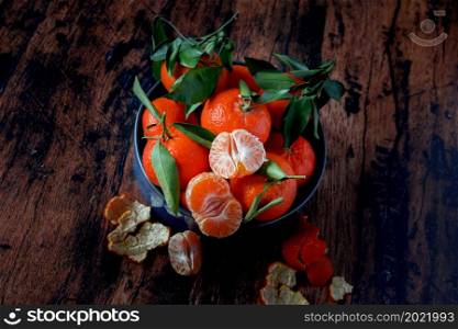 Clementines with leaves in a blue ceramic dish on an old wooden table