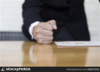 clenched fist of businessman on office desk - angry and furious business concept - blur for use as background