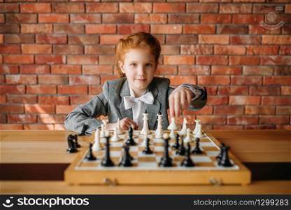 Clever schoolgirl, chess player at the table. Young girl at the chessboard, female kid plays logic game