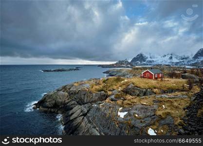 Clif with traditional red rorbu house on Litl-Toppoya islet on Lofoten Islands, Norway in winter. Clif with traditional red rorbu house on Lofoten Islands, Norway