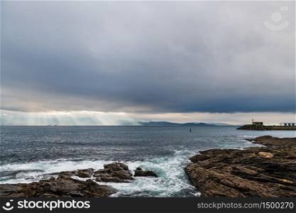 Cliffs and small lighthouse on a cloudy Winter day in Portonovo in Galicia, Spain, with the entrance to the Ria de Pontevedra in the background.