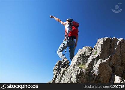 Climber pointing to somewhere over deep blue sky; horizontal frame.
