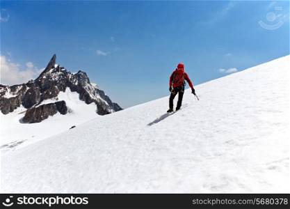 Climber standing on a glacier looking at a mountain peak. Dent du Geant, Mont Blanc, Chamonix, France.