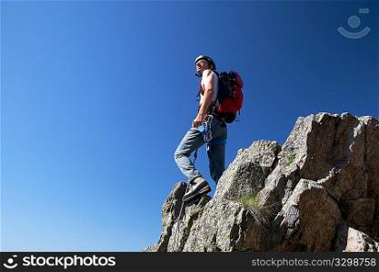 Climber standing on a stone at the top of his route, over a deep blue sky.