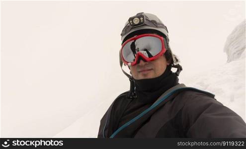 Climber with helmet, headl&and black jacket taking a selfie on a glacier on a cloudy day, landscape reflected in red framed glasses. Climber with helmet, headl&and black jacket taking a selfie on a glacier on a cloudy day