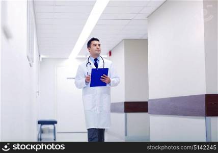 clinic, people, health care and medicine concept - doctor with clipboard walking along hospital corridor. doctor with clipboard walking along hospital
