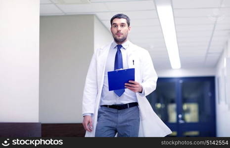 clinic, people, health care and medicine concept - doctor with clipboard walking along hospital corridor. doctor with clipboard walking along hospital