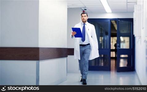 clinic, people, health care and medicine concept - doctor with clipboard walking along hospital corridor. doctor with clipboard walking along hospital