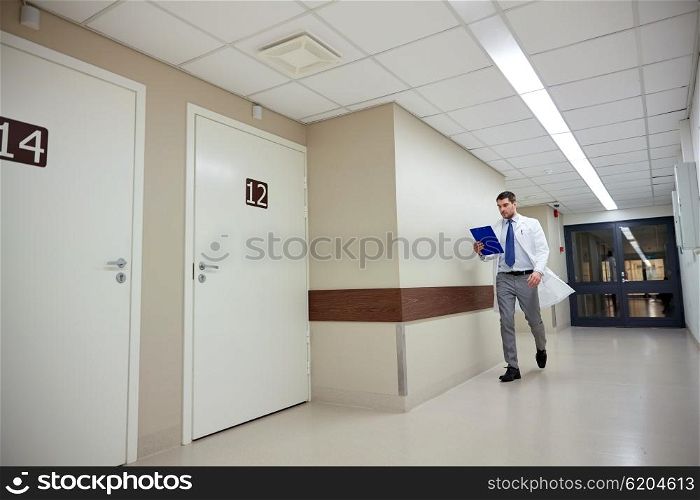 clinic, people, health care and medicine concept - doctor with clipboard walking along hospital corridor