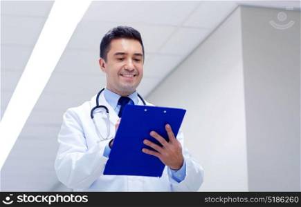 clinic, people, health care and medicine concept - smiling doctor with clipboard at hospital corridor. smiling doctor with clipboard at hospital corridor
