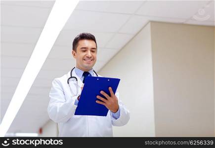 clinic, people, health care and medicine concept - smiling doctor with clipboard at hospital corridor