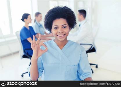 clinic, profession, people and medicine concept - happy african american female doctor over group of medics meeting at hospital showing ok hand sign