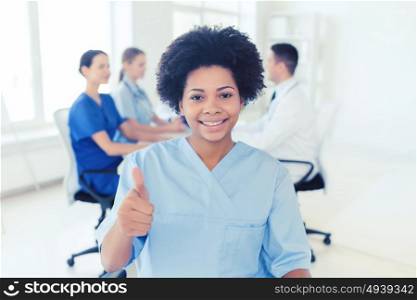 clinic, profession, people and medicine concept - happy african american female doctor or nurse over group of medics meeting at hospital showing thumbs up gesture. happy female doctor or nurse showing thumbs up