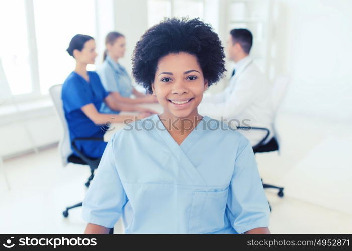 clinic, profession, people and medicine concept - happy african american female doctor or nurse over group of medics meeting at hospital. doctor or nurse over group of medics at hospital