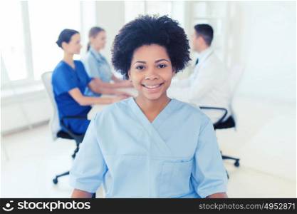 clinic, profession, people and medicine concept - happy african american female doctor or nurse over group of medics meeting at hospital. doctor or nurse over group of medics at hospital