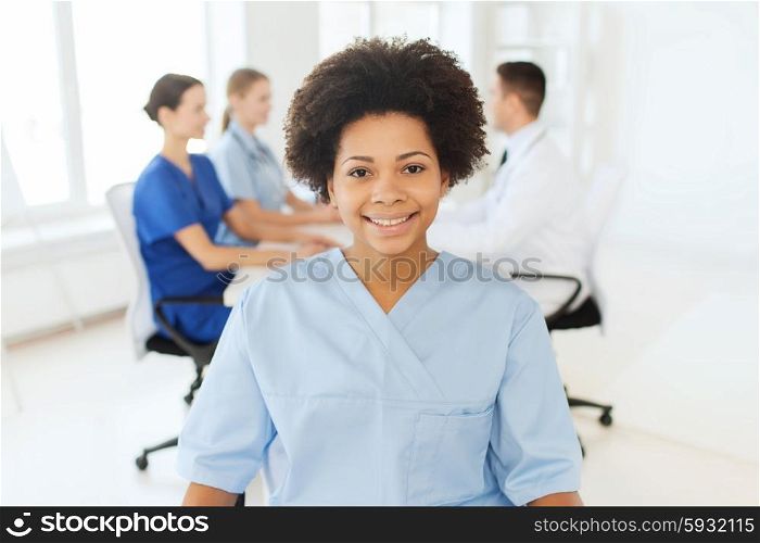 clinic, profession, people and medicine concept - happy african american female doctor or nurse over group of medics meeting at hospital