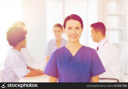 clinic, profession, people and medicine concept - happy female doctor or nurse over group of medics meeting at hospital