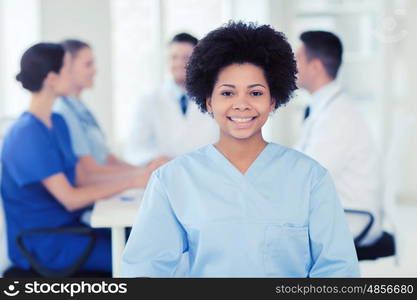 clinic, profession, people and medicine concept - happy female doctor or nurse over group of medics meeting at hospital