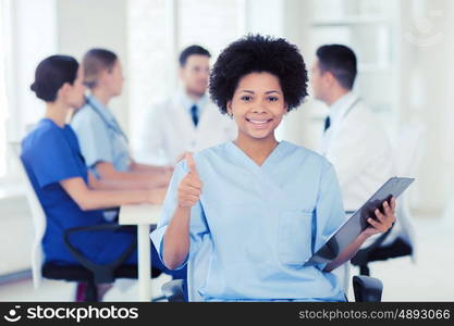 clinic, profession, people and medicine concept - happy female doctor or nurse with clipboard over group of medics meeting at hospital showing thumbs up gesture