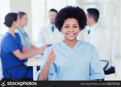 clinic, profession, people and medicine concept - happy female doctor or nurse over group of medics meeting at hospital showing thumbs up gesture. happy doctor over group of medics at hospital