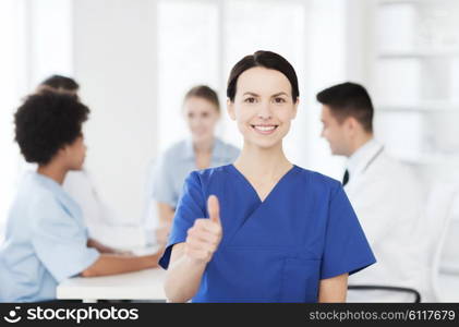 clinic, profession, people and medicine concept - happy female doctor or nurse over group of medics meeting at hospital showing thumbs up gesture