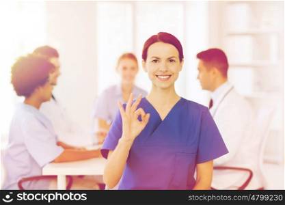 clinic, profession, people and medicine concept - happy female doctor over group of medics meeting at hospital showing ok hand sign