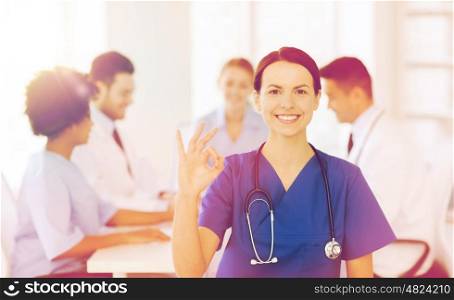 clinic, profession, people and medicine concept - happy female doctor over group of medics meeting at hospital showing ok hand sign