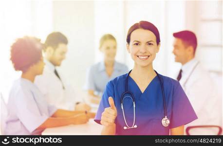 clinic, profession, people and medicine concept - happy female doctor over group of medics meeting at hospital showing thumbs up gesture