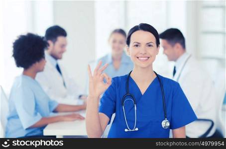 clinic, profession, people and medicine concept - happy female doctor over group of medics meeting at hospital showing ok hand sign. happy doctor over group of medics at hospital