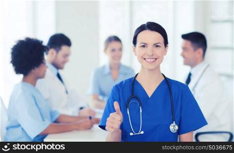 clinic, profession, people and medicine concept - happy female doctor over group of medics meeting at hospital showing thumbs up gesture. happy doctor over group of medics at hospital