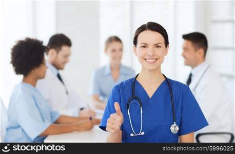 clinic, profession, people and medicine concept - happy female doctor over group of medics meeting at hospital showing thumbs up gesture
