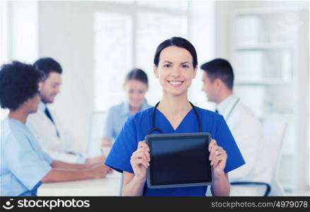 clinic, profession, people and medicine concept - happy female doctor showing tablet pc computer blank screen over group of medics meeting at hospital. happy doctor over group of medics at hospital